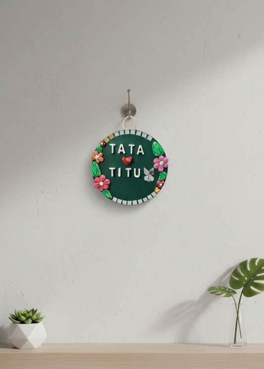 Decorative sign with 'TATA TITU' text on a white wall with plants.