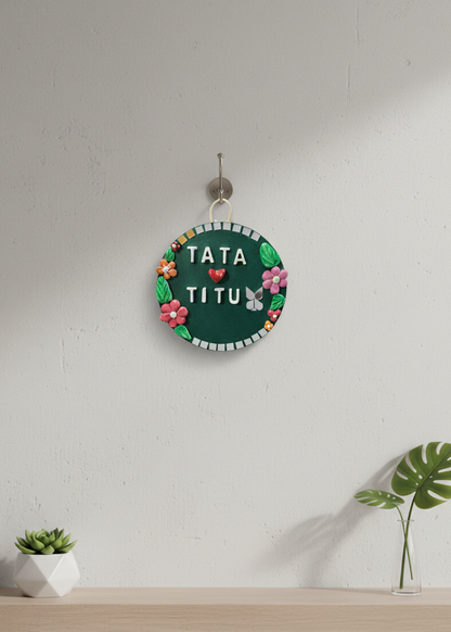 Decorative sign with 'TATA TITU' text on a white wall with plants.